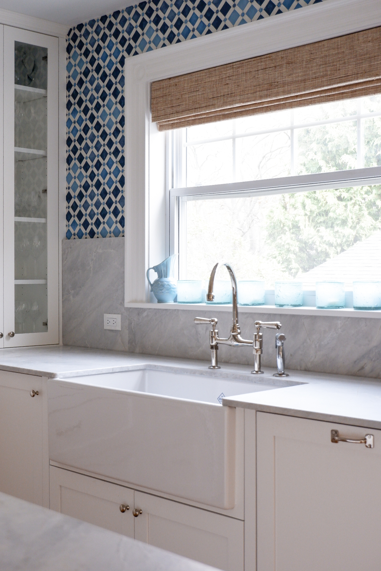 White inset cabinetry with a farmhouse sink, marble counters, and blue tile