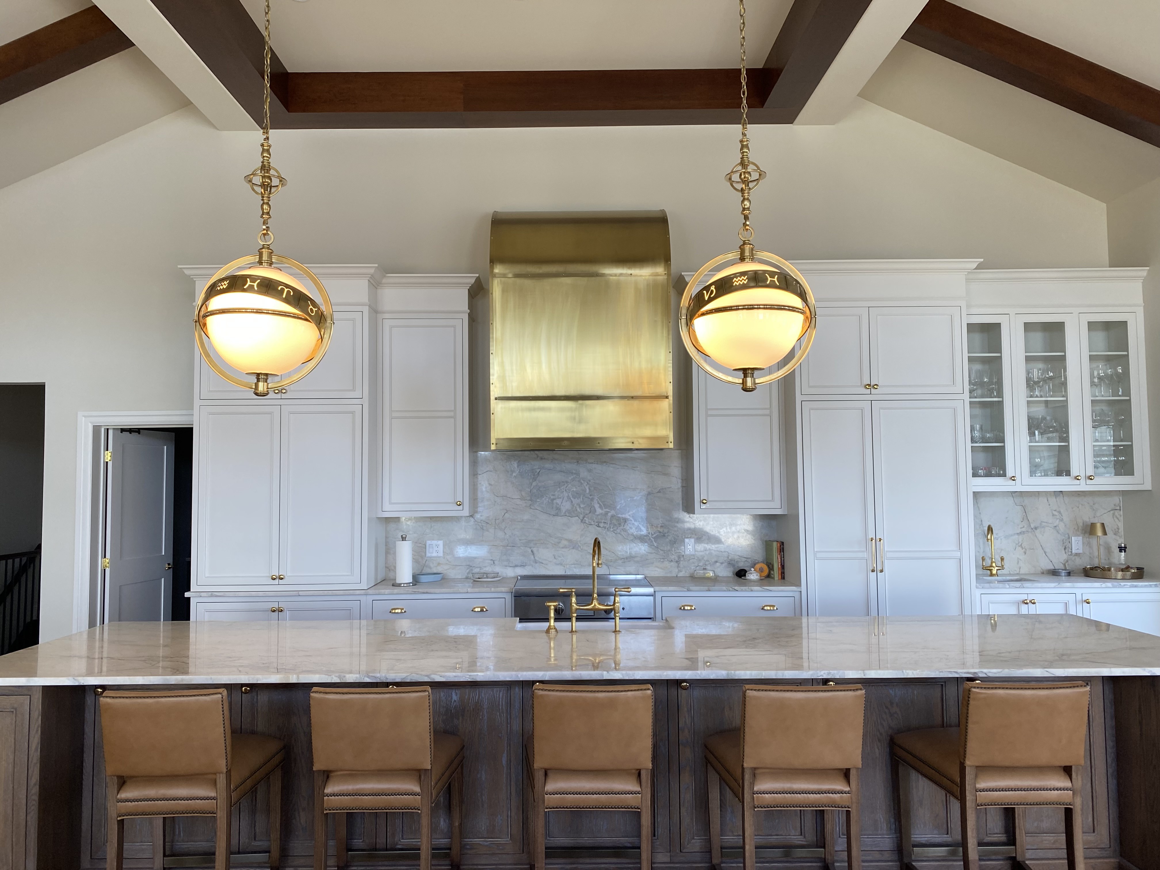 Custom white kitchen with a brass range hood, marble surfaces, and stained oak island by Hempston