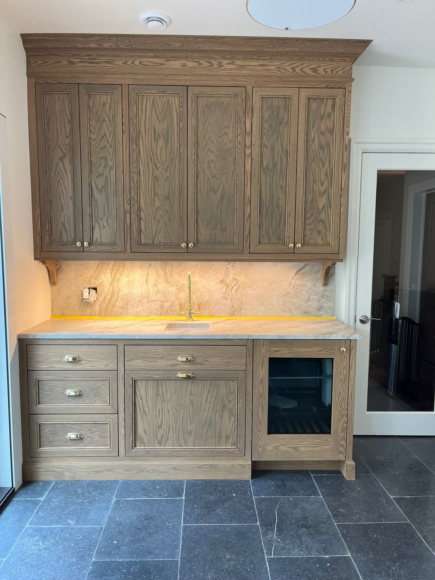 Grey-stained white oak bar and pantry cabinetry with brass hardware